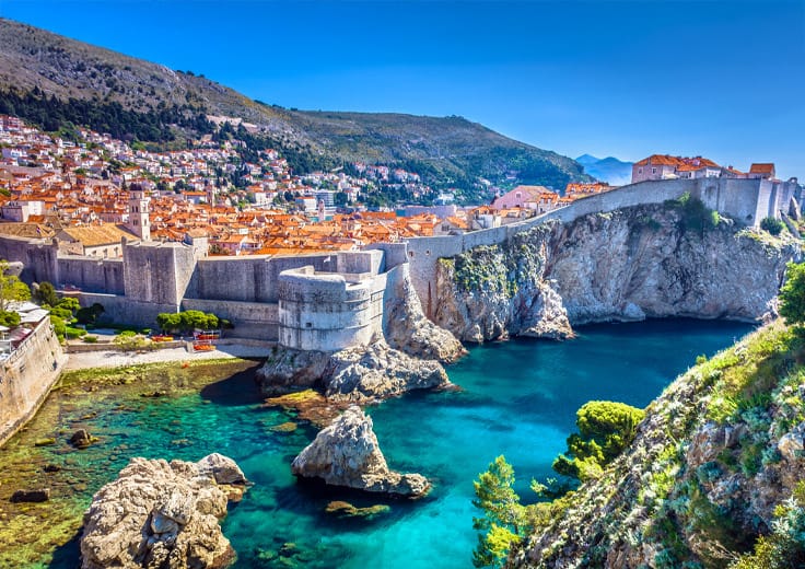 Panoramic view of Dubrovnik's Old Town, showcasing its medieval city walls, terracotta rooftops, and the azure Adriatic Sea in the background.