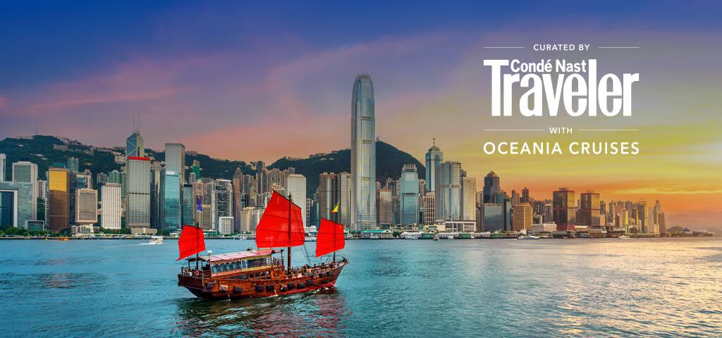 Traditional red-sailed junk boat sailing across Victoria Harbour with the Hong Kong skyline and a golden sunset in the background.